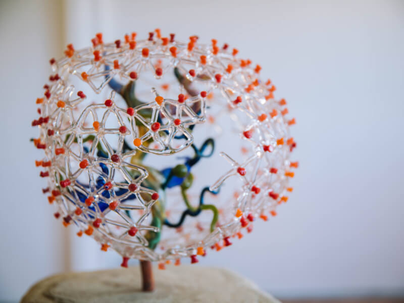 A piece of hand blown glass art with red and orange points and clear webs.